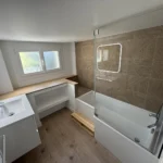 Rénovation complète d’une salle de bain à Galluis (78) : baignoire avec pare-bain, faïence effet bois et fenêtre neuve, par ABRP