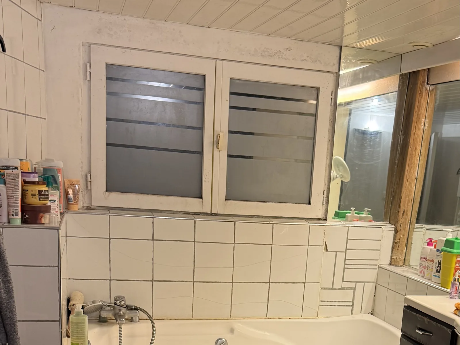 Salle de bain avant travaux à Galluis : baignoire, faïence blanche et ancienne fenêtre à carreaux
