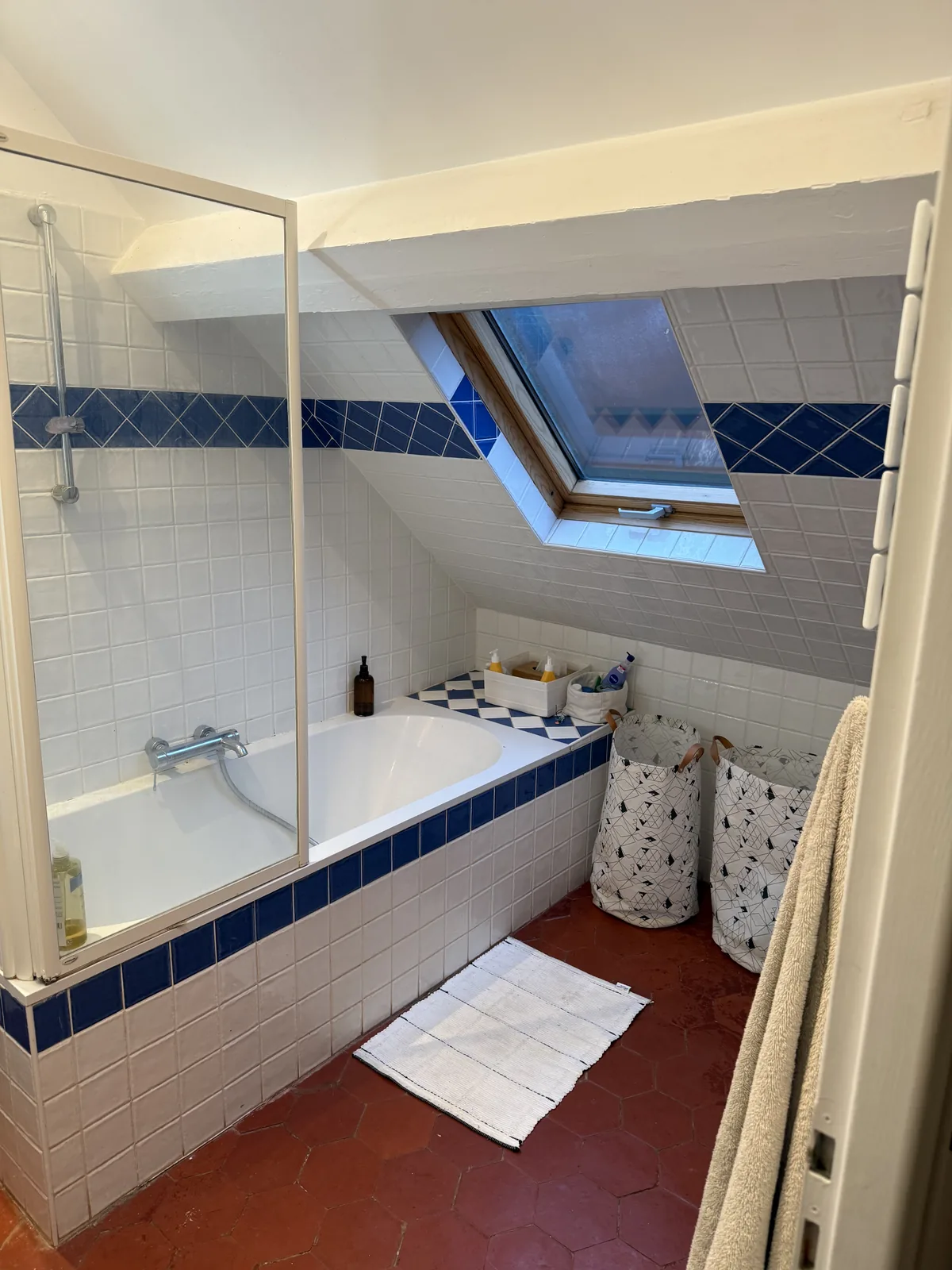 Salle de bains avant travaux à Grosrouvre : baignoire sous les combles et faïence blanche à frise bleue
