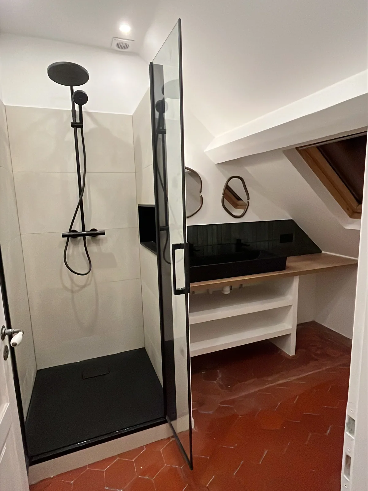 Vue générale de la salle de bains rénovée à Grosrouvre : douche, meuble vasque et tomettes conservées